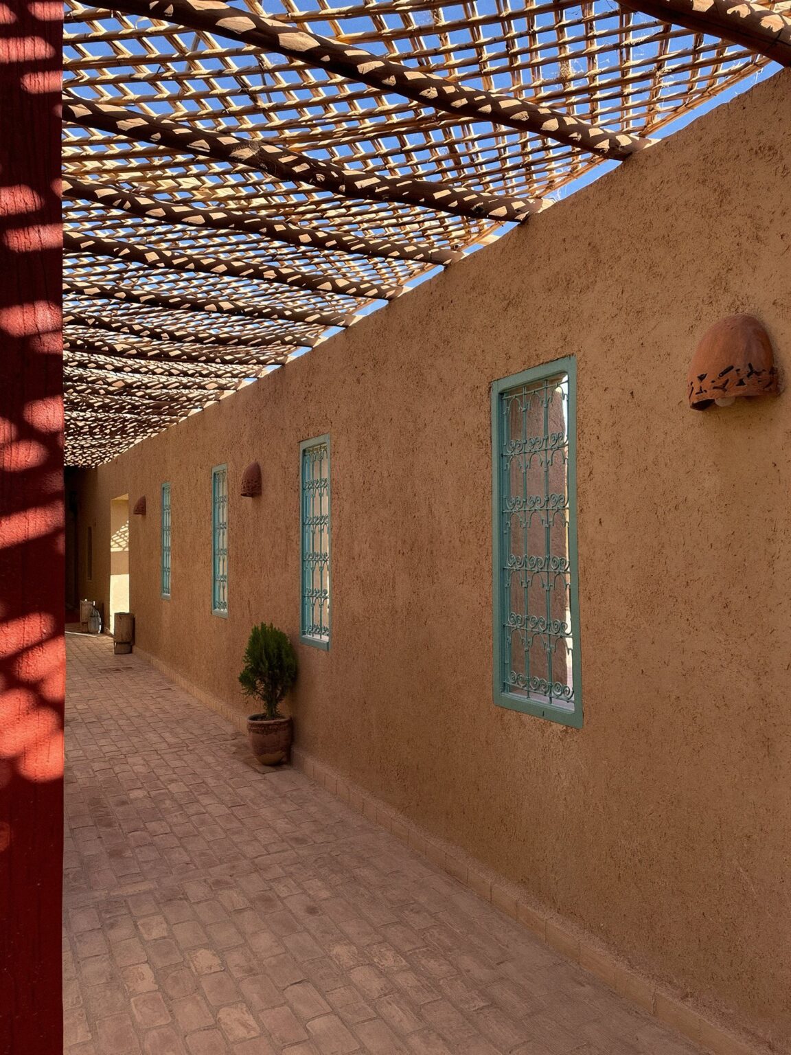 Outdoor corridor with reed roof and turquoise windows at Dar el Janoub